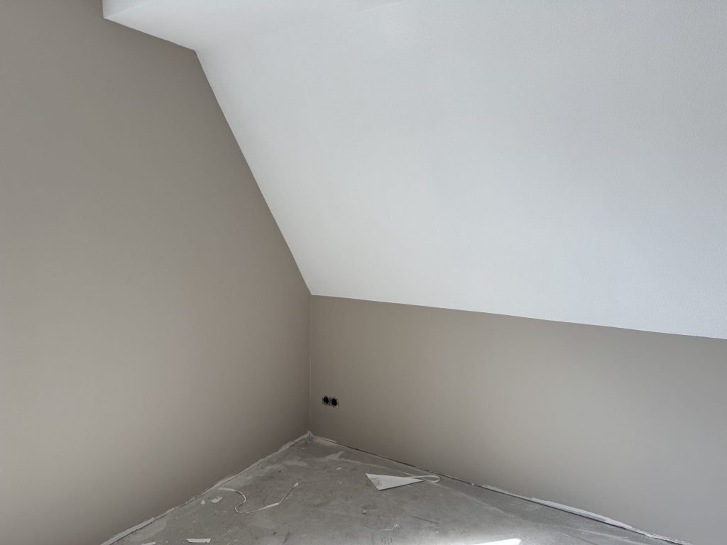 Zolderkamer van een nieuwbouwhuis met een schuine wand in wit en rechte wanden in een zachte beige tint