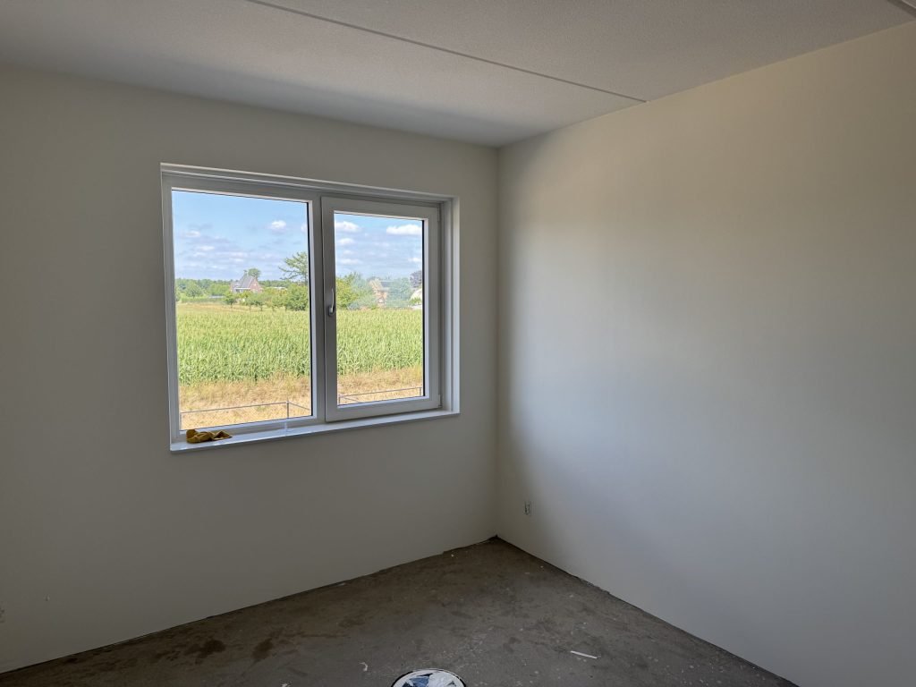 Lege nieuwe kamer met gladde, lichte wanden, een betonvloer en een raam met uitzicht over het land